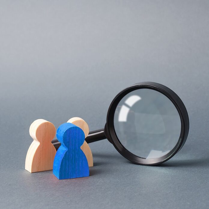Three wooden human figure stands near a magnifying glass on a gray background. Search for vacancies and work. Human resources, management. The concept of the search for people and workers. Recruitment